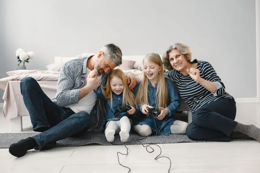 Two grandparents on the floor with two young girls who are laughing and holding game controllers